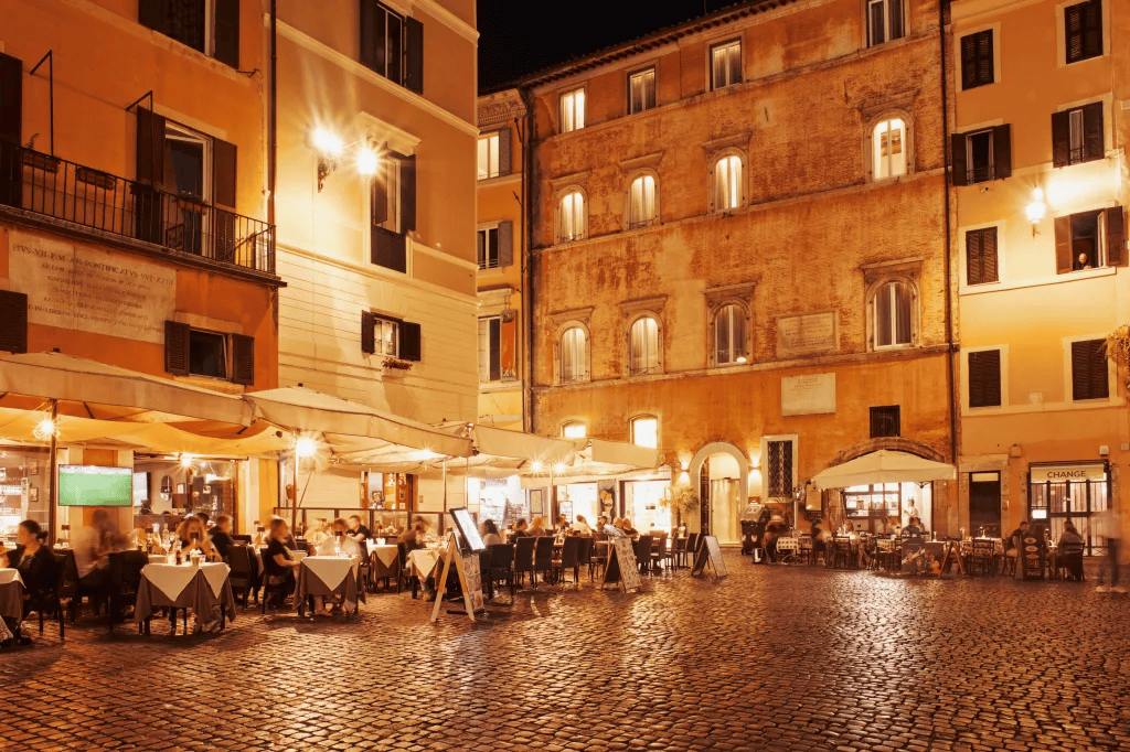 Trastevere in Rome, Italy, during the evening with the lights turned on and the outdoor sitting area shining in the evening.