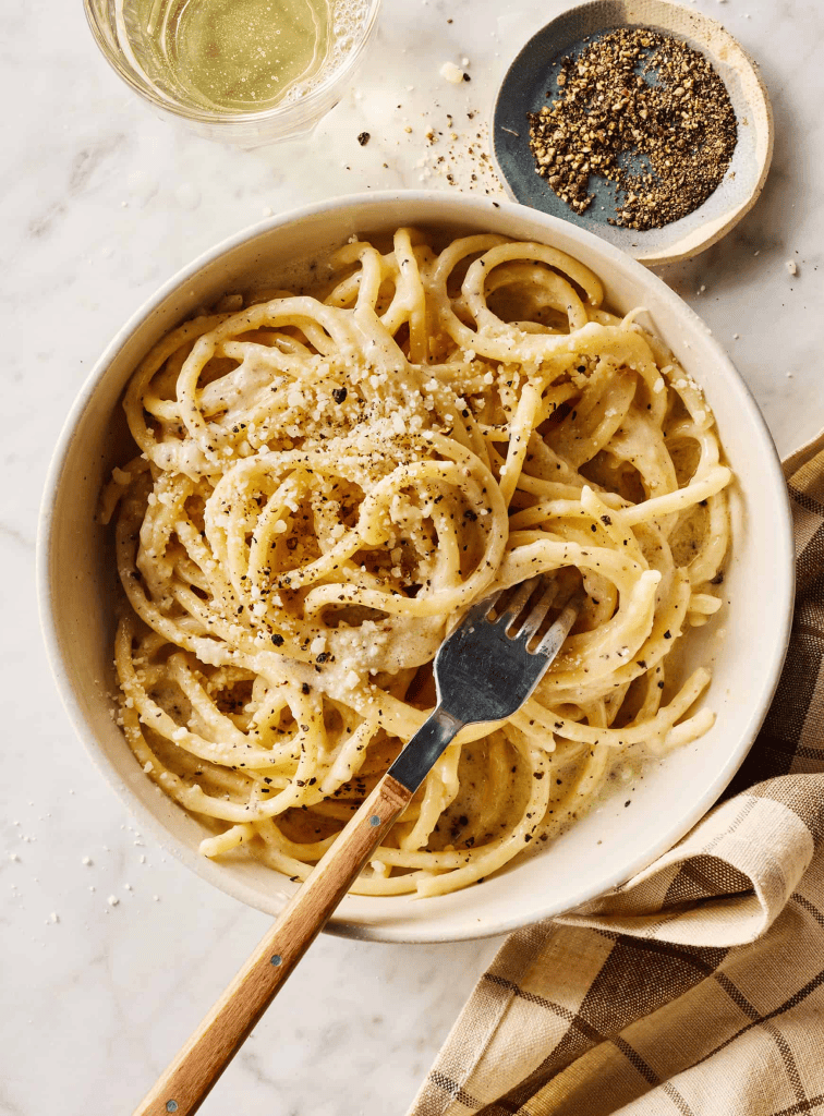 Italian cacio e pepe on a white plate with a fork and linnen.