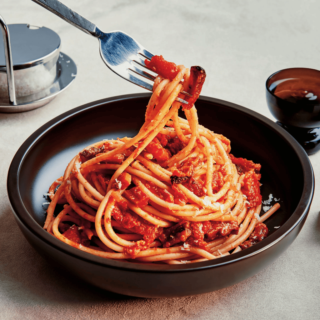 Italian amatriciana in a black bowl with a fork lifting up the food.